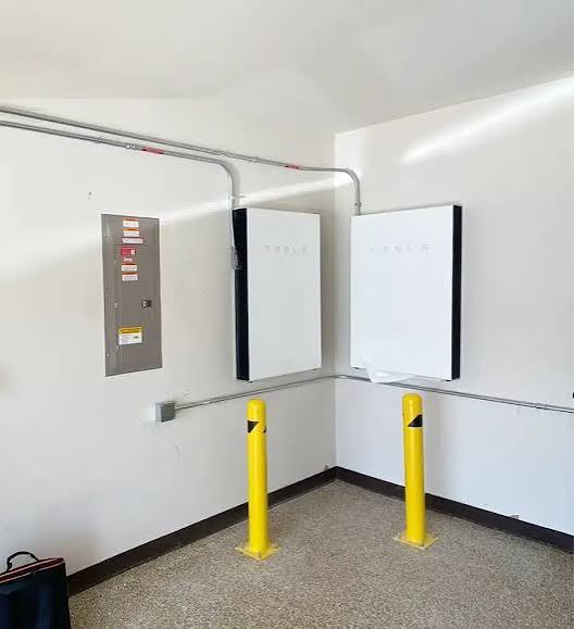Two Tesla Powerwall home batteries on a commercial wall with safety bollards