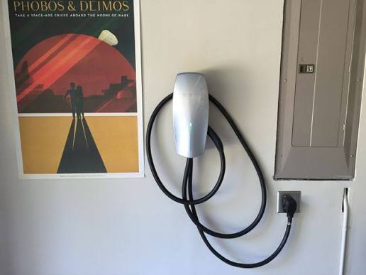 Silver Tesla Wall Connector on a garage wall next to the electrical panel